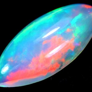 May include: A polished, oval-shaped opal gemstone. The opal displays a play of color with vibrant hues of blue, green, and red. The gemstone is set against a black background, highlighting its iridescent qualities.