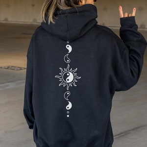Op de afbeelding: Zwart hoodie met een wit yin yang symbool en een zon ontwerp op de rug.