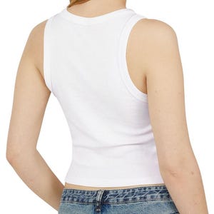 May include: A white, sleeveless crop top with a scoop neckline. The ribbed tank top is made of a soft material and is visible from the back. The bottom of the top is cropped, and the model is wearing blue jeans.