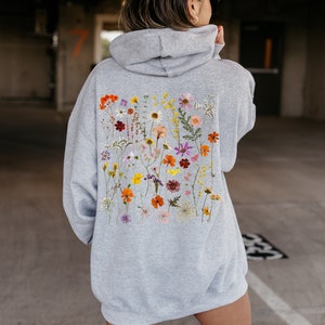 May include: A gray hoodie with a floral print on the back. The print features a variety of dried flowers in shades of pink, orange, yellow, and purple.