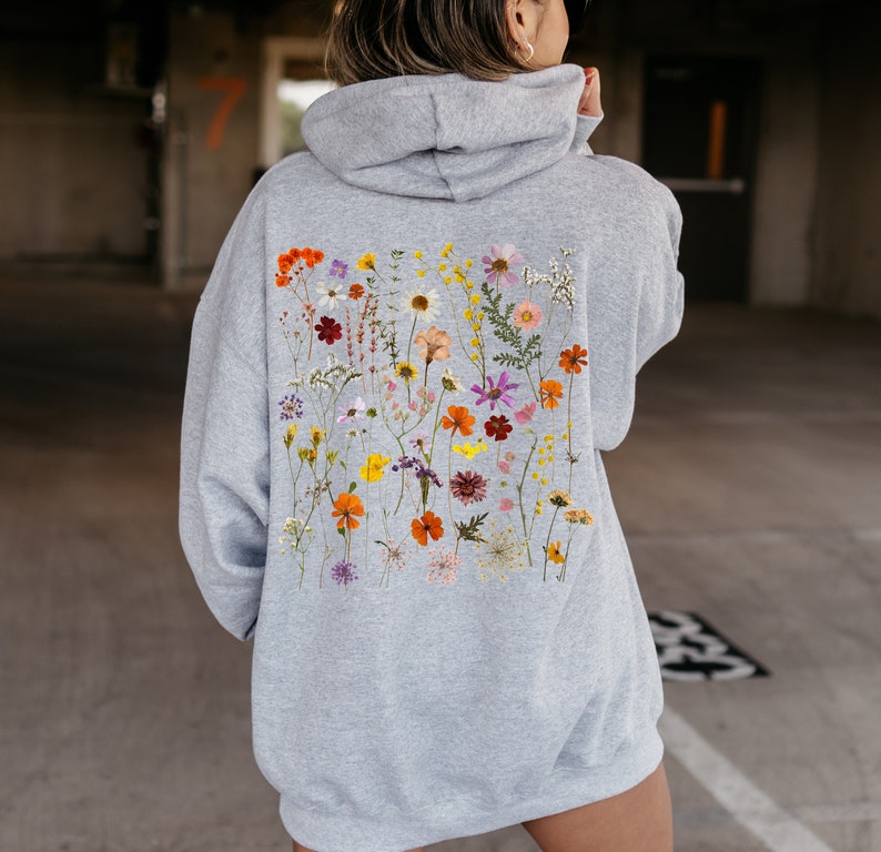 May include: A gray hoodie with a floral print on the back. The print features a variety of dried flowers in shades of pink, orange, yellow, and purple.