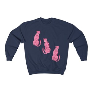 May include: A navy blue sweatshirt with a pink leopard print design. The design features three leopards sitting in a row.