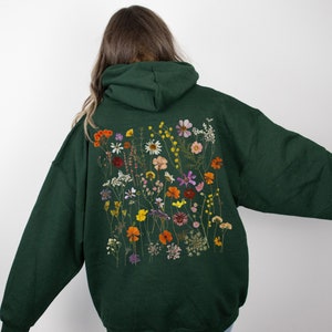 May include: A dark green hoodie with a large floral print on the back. The print features a variety of dried flowers in shades of orange, yellow, pink, and purple.