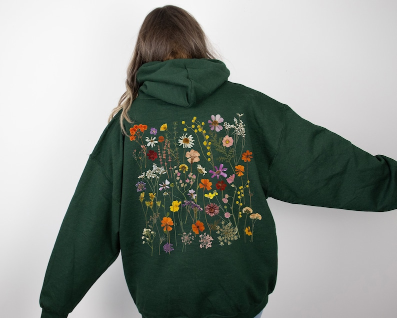 May include: A dark green hoodie with a large floral print on the back. The print features a variety of dried flowers in shades of orange, yellow, pink, and purple.