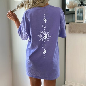 Puede incluir: Una camiseta de gran tama&ntilde;o de color morado con un s&iacute;mbolo yin yang blanco dentro de un gr&aacute;fico de sol y s&iacute;mbolos yin yang m&aacute;s peque&ntilde;os arriba y abajo.