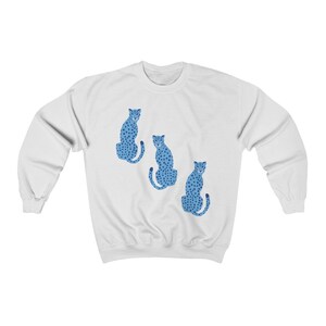May include: White sweatshirt with a blue cheetah print design. Three cheetahs are sitting in a row on the front of the sweatshirt.