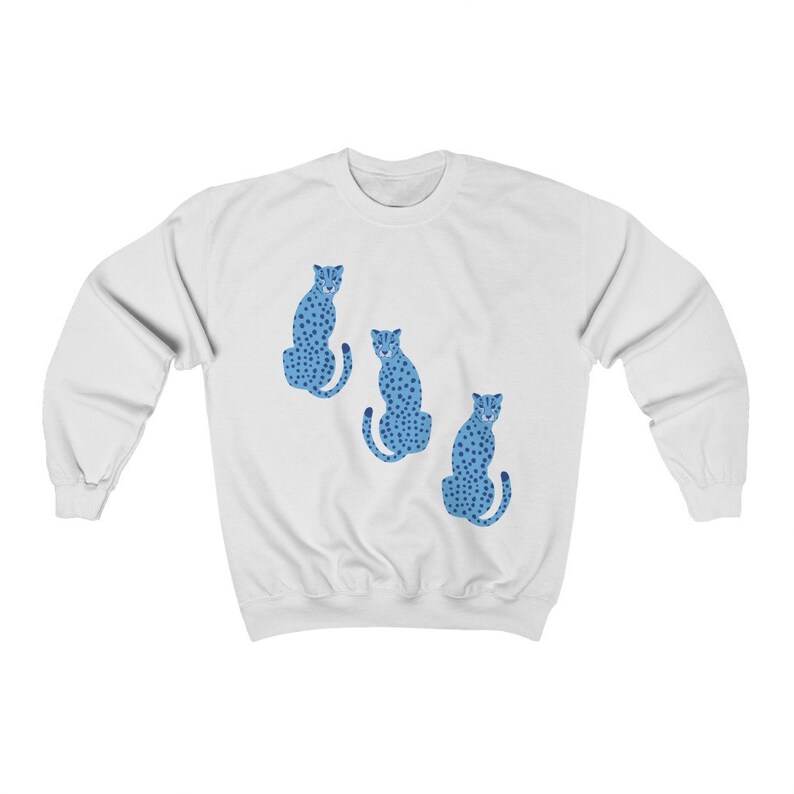 May include: White sweatshirt with a blue cheetah print design. Three cheetahs are sitting in a row on the front of the sweatshirt.