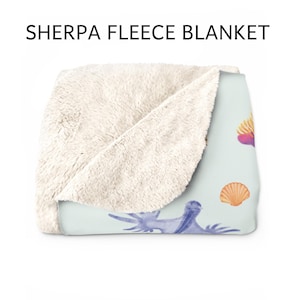 May include: Sherpa fleece blanket with a light blue background and a seashell design. The blanket features a soft, cream-colored sherpa fleece on one side and a printed design on the other. The design includes watercolor illustrations of seashells and sea creatures.