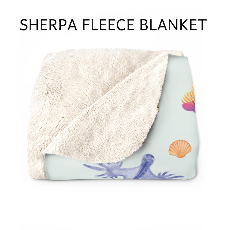 May include: Sherpa fleece blanket with a light blue background and a seashell design. The blanket features a soft, cream-colored sherpa fleece on one side and a printed design on the other. The design includes watercolor illustrations of seashells and sea creatures.