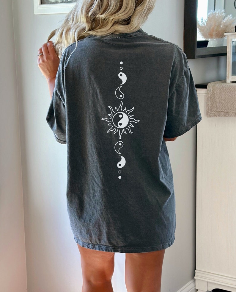 Puede incluir: Una camiseta gris oscura de gran tama&ntilde;o con un s&iacute;mbolo yin yang blanco y un dise&ntilde;o de sol en la espalda.