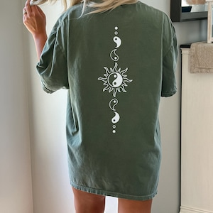 Puede incluir: Una camiseta verde de gran tama&ntilde;o con un s&iacute;mbolo yin yang blanco dentro de un gr&aacute;fico de sol en la espalda.