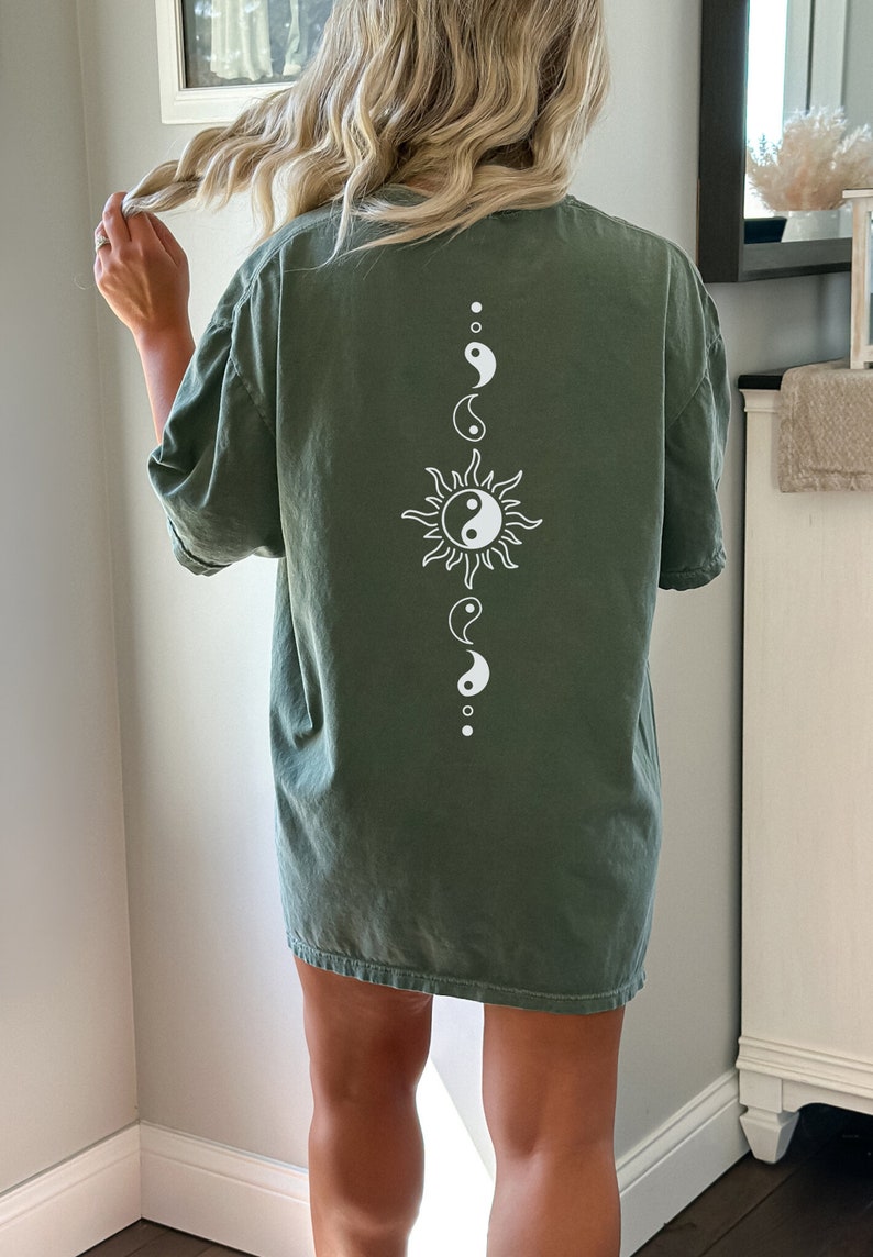 Puede incluir: Una camiseta verde de gran tama&ntilde;o con un s&iacute;mbolo yin yang blanco dentro de un gr&aacute;fico de sol en la espalda.