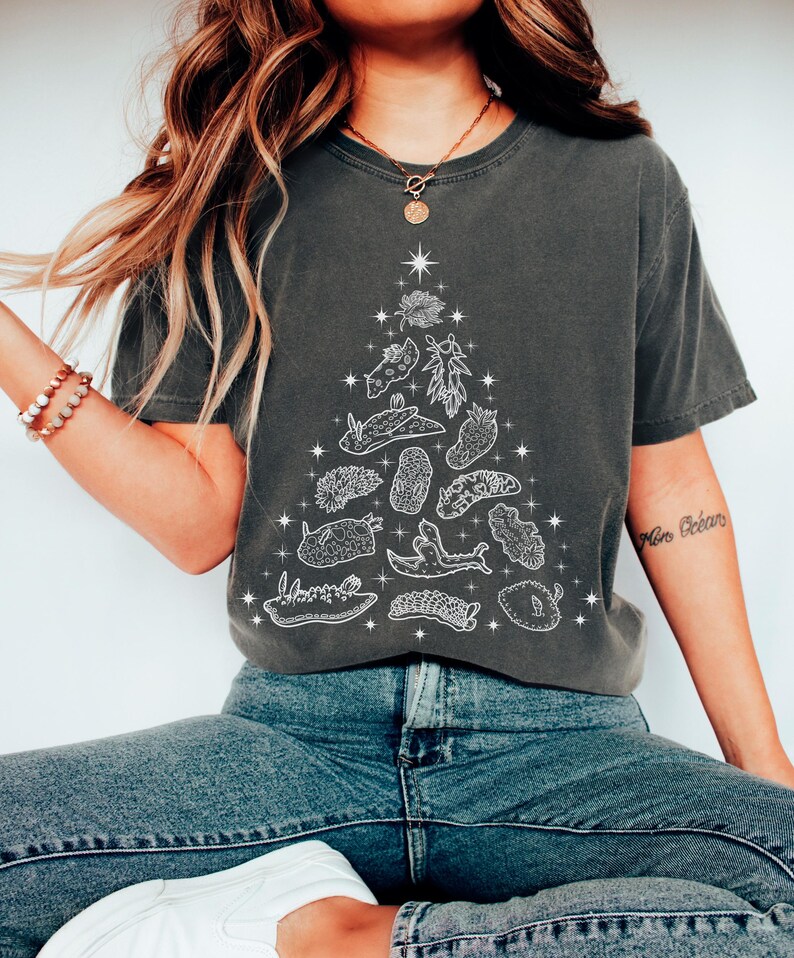 May include: Dark gray t-shirt featuring a white illustration of a Christmas tree made of various sea creatures and plants. The design includes starfish and other aquatic life. The shirt is a comfortable, casual style.