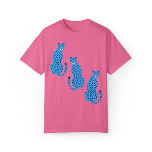 K&ouml;nnte beinhalten: Ein pinkfarbenes T-Shirt mit einem Motiv von drei blauen Geparden mit schwarzen Flecken, die in einer Reihe sitzen.