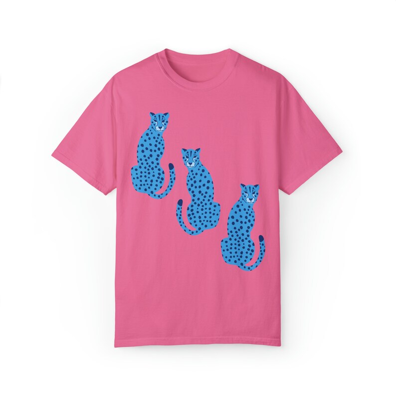 K&ouml;nnte beinhalten: Ein pinkfarbenes T-Shirt mit einem Motiv von drei blauen Geparden mit schwarzen Flecken, die in einer Reihe sitzen.