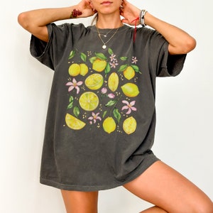 May include: A dark gray oversized t-shirt with a lemon print. The lemons are yellow with green leaves and pink flowers.