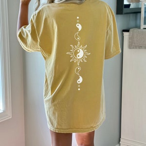 Puede incluir: Una camiseta amarilla de gran tama&ntilde;o con un dise&ntilde;o de sol blanco y s&iacute;mbolo yin yang en la espalda.
