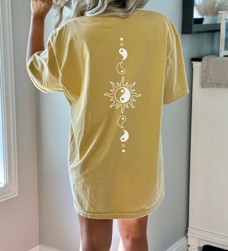 Puede incluir: Una camiseta amarilla de gran tama&ntilde;o con un dise&ntilde;o de sol blanco y s&iacute;mbolo yin yang en la espalda.