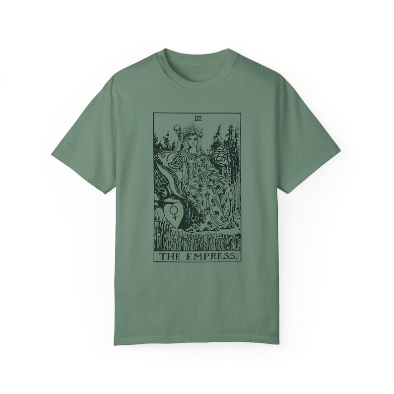 May include: A green t-shirt with a black and white illustration of the Empress tarot card. The card shows a woman sitting on a throne with a crown on her head. The text "III THE EMPRESS." is printed below the image.