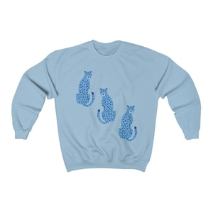 May include: A light blue sweatshirt with a graphic of three blue cheetahs with black spots. The cheetahs are sitting down and facing forward.