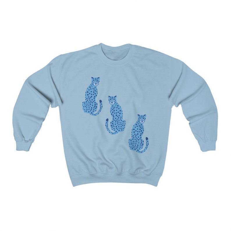 May include: A light blue sweatshirt with a graphic of three blue cheetahs with black spots. The cheetahs are sitting down and facing forward.