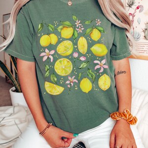 May include: A green t-shirt with a lemon print. The lemons are yellow and the leaves are green. There are also pink flowers on the shirt.
