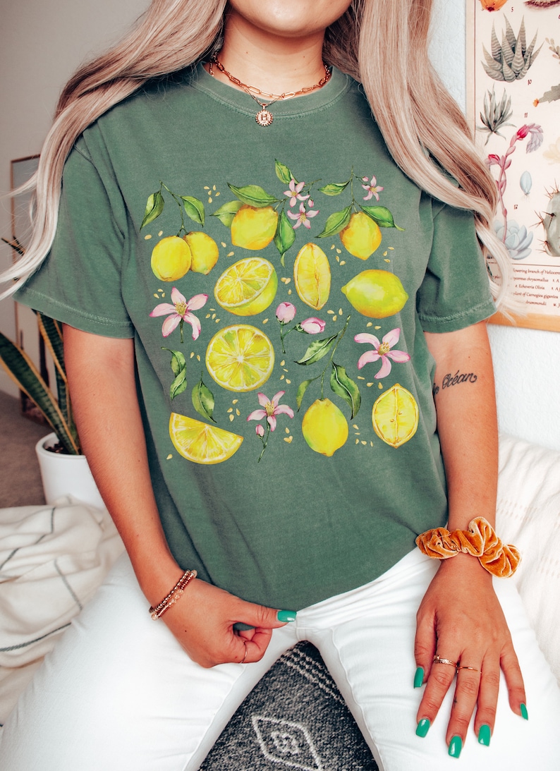 May include: A green t-shirt with a lemon print. The lemons are yellow and the leaves are green. There are also pink flowers on the shirt.