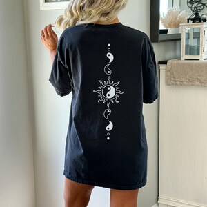 Puede incluir: Camiseta negra de gran tama&ntilde;o con un s&iacute;mbolo yin yang blanco y un gr&aacute;fico de sol en la espalda.