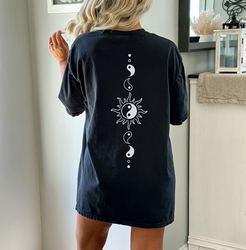Puede incluir: Camiseta negra de gran tama&ntilde;o con un s&iacute;mbolo yin yang blanco y un gr&aacute;fico de sol en la espalda.