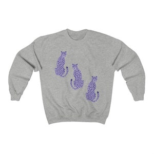 May include: A gray sweatshirt with a purple cheetah print design. Three cheetahs are sitting in a row on the front of the sweatshirt.