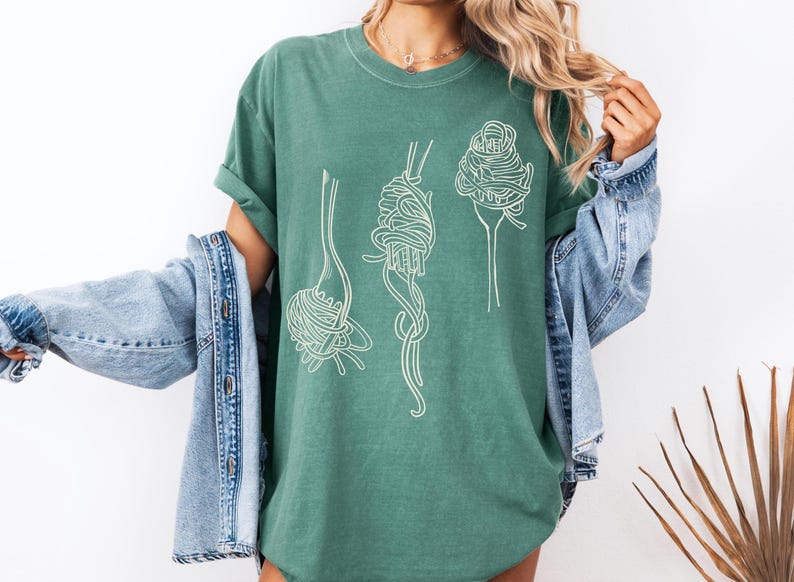 K&ouml;nnte beinhalten: Ein gr&uuml;nes T-Shirt mit einer wei&szlig;en Grafik von drei Gabeln mit Spaghetti darauf.