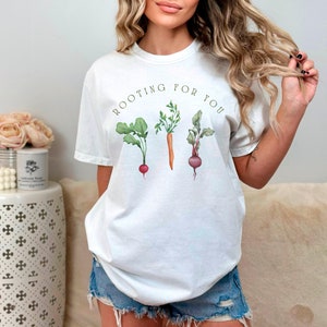 May include: White t-shirt with the text "ROOTING FOR YOU" and a graphic of three vegetables: a radish, a carrot, and a beet.