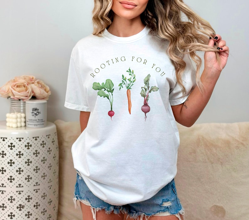 May include: White t-shirt with the text "ROOTING FOR YOU" and a graphic of three vegetables: a radish, a carrot, and a beet.