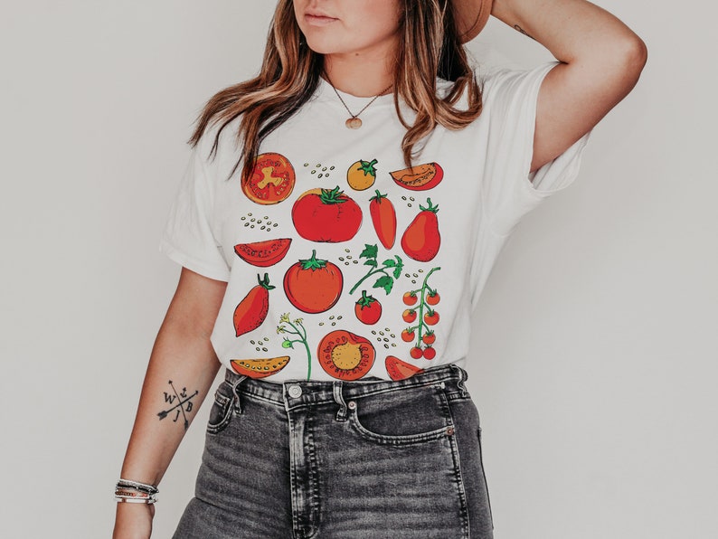 May include: White t-shirt with a colourful tomato print. The print features red, orange, and green tomatoes in various shapes and sizes.