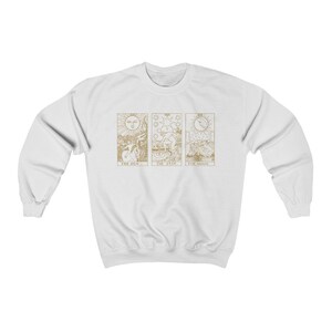 K&ouml;nnte beinhalten: Wei&szlig;es Sweatshirt mit goldenen Tarotkarten-Designs. Die Karten sind "Die Sonne", "Der Stern" und "Der Mond". Das Sweatshirt hat einen Rundhalsausschnitt und lange &Auml;rmel.