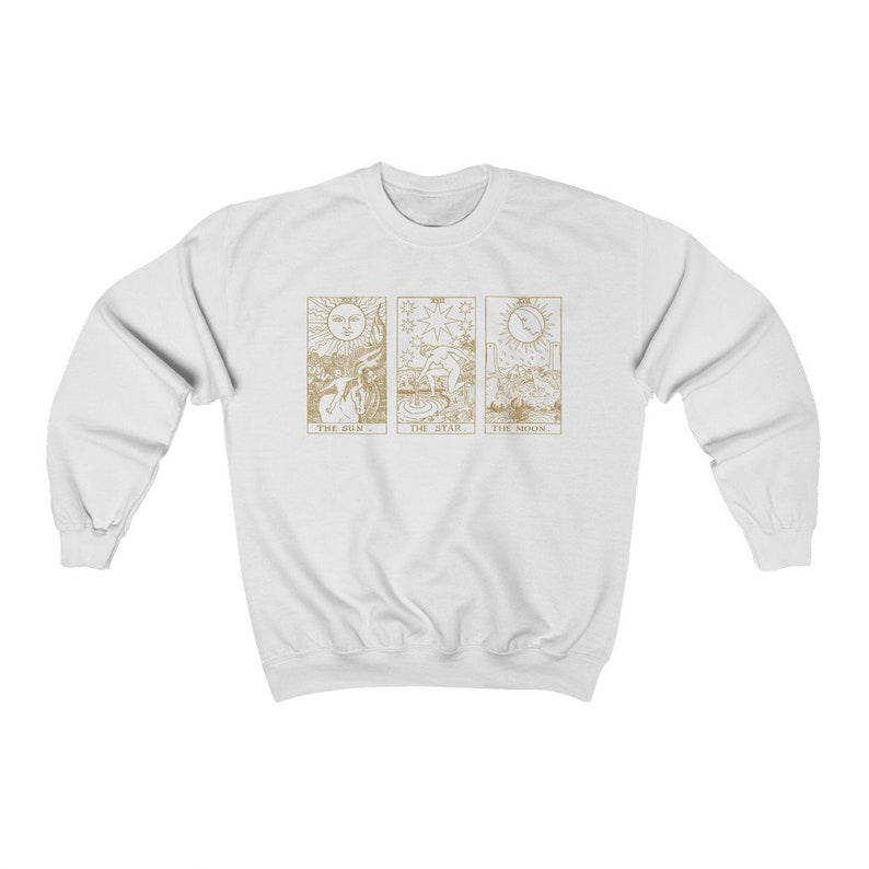 K&ouml;nnte beinhalten: Wei&szlig;es Sweatshirt mit goldenen Tarotkarten-Designs. Die Karten sind "Die Sonne", "Der Stern" und "Der Mond". Das Sweatshirt hat einen Rundhalsausschnitt und lange &Auml;rmel.