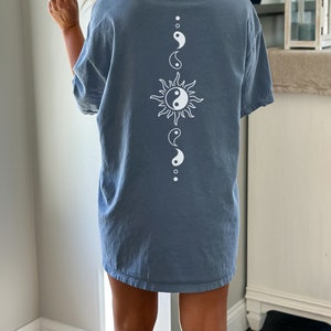 Puede incluir: Una camiseta azul con un s&iacute;mbolo yin yang blanco y un gr&aacute;fico de sol en la espalda.