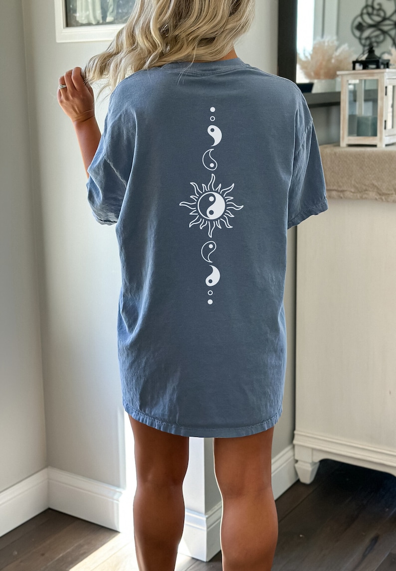 Puede incluir: Una camiseta azul con un s&iacute;mbolo yin yang blanco y un gr&aacute;fico de sol en la espalda.