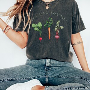 May include: A dark gray t-shirt with a graphic of a carrot, a beet, and a radish with the text "Rooting for you".
