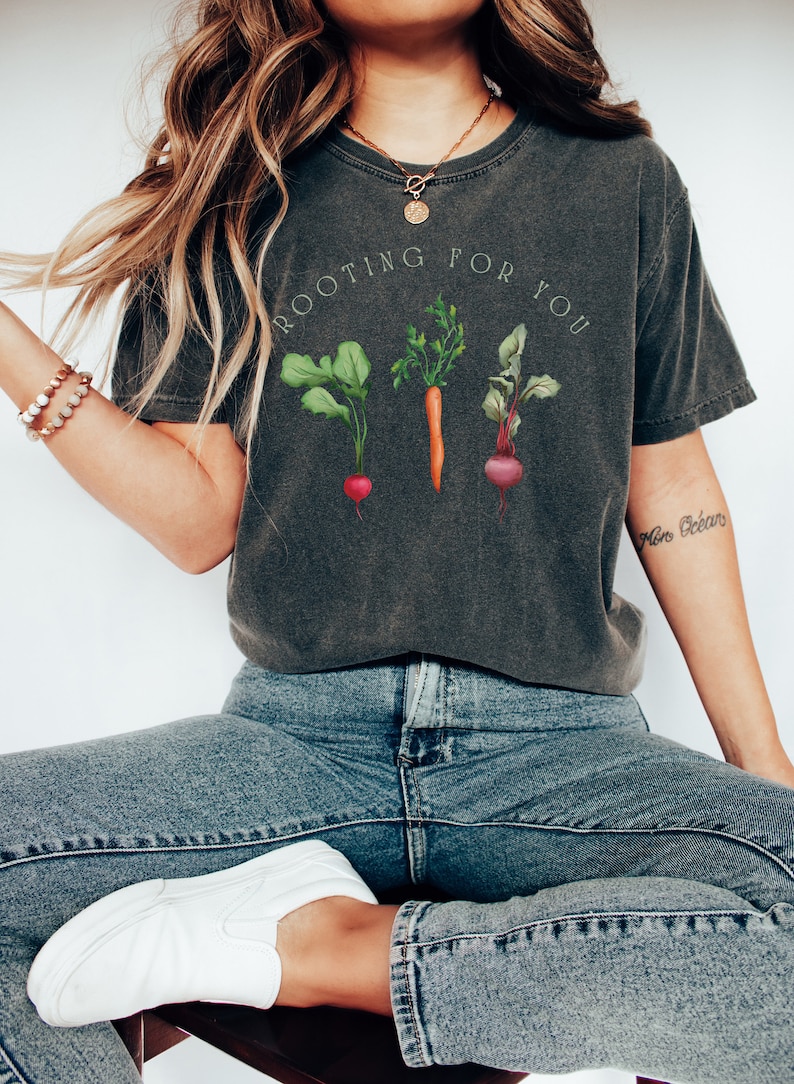 May include: A dark gray t-shirt with a graphic of a carrot, a beet, and a radish with the text "Rooting for you".