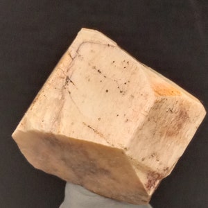 Puede incluir: Un gran cristal facetado de color marrón claro con una superficie rugosa y texturizada. El cristal tiene un tono ligeramente anaranjado y es translúcido.