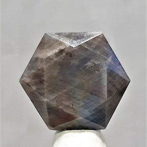 May include: A faceted, hexagonal, gray and blue gemstone with a star-like pattern.