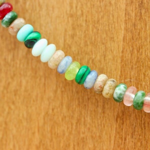 May include: A strand of colorful gemstone beads in various shapes and sizes. The beads include shades of red, green, blue, yellow, and purple. The beads are strung together, creating a vibrant and eye-catching accessory.