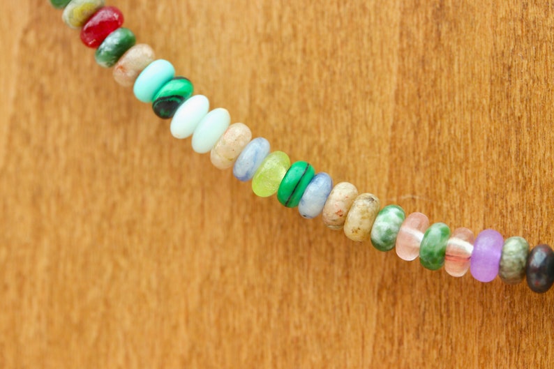 May include: A strand of colorful gemstone beads in various shapes and sizes. The beads include shades of red, green, blue, yellow, and purple. The beads are strung together, creating a vibrant and eye-catching accessory.