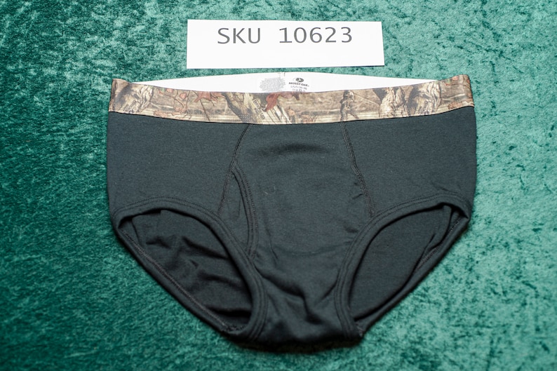 May include: Black briefs with a camouflage waistband. The briefs are made of a soft material and have a classic design. The waistband features a brown and green camouflage pattern. SKU 10623 is printed on a white label.