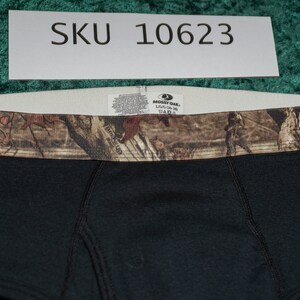 May include: Black boxer briefs with a camouflage waistband. The briefs have a tag that reads "Mossy Oak" and "L/G (36-38)". The SKU number "10623" is visible on a white label above the briefs.