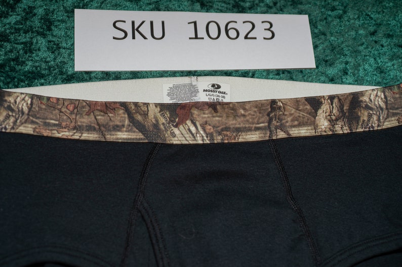 May include: Black boxer briefs with a camouflage waistband. The briefs have a tag that reads "Mossy Oak" and "L/G (36-38)". The SKU number "10623" is visible on a white label above the briefs.