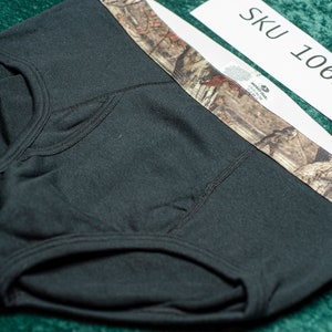 May include: Black briefs with a camouflage waistband. The briefs are made of a soft material and feature a classic brief design. The tag reads "SKU 10623".