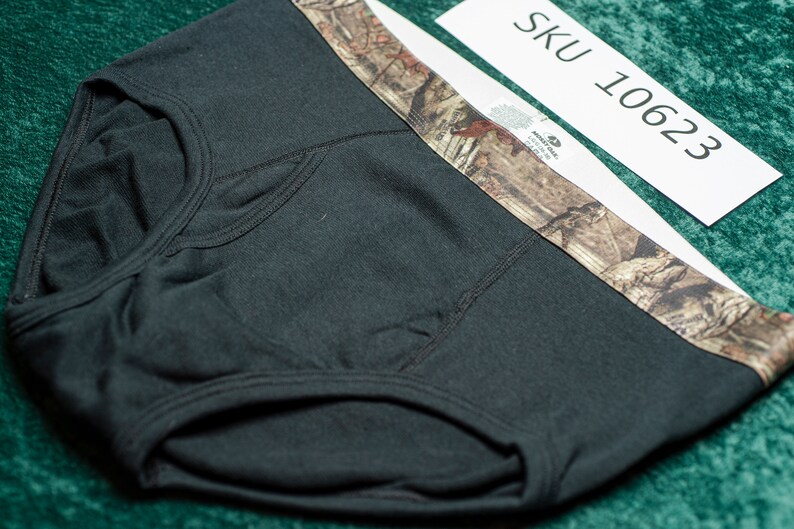 May include: Black briefs with a camouflage waistband. The briefs are made of a soft material and feature a classic brief design. The tag reads "SKU 10623".