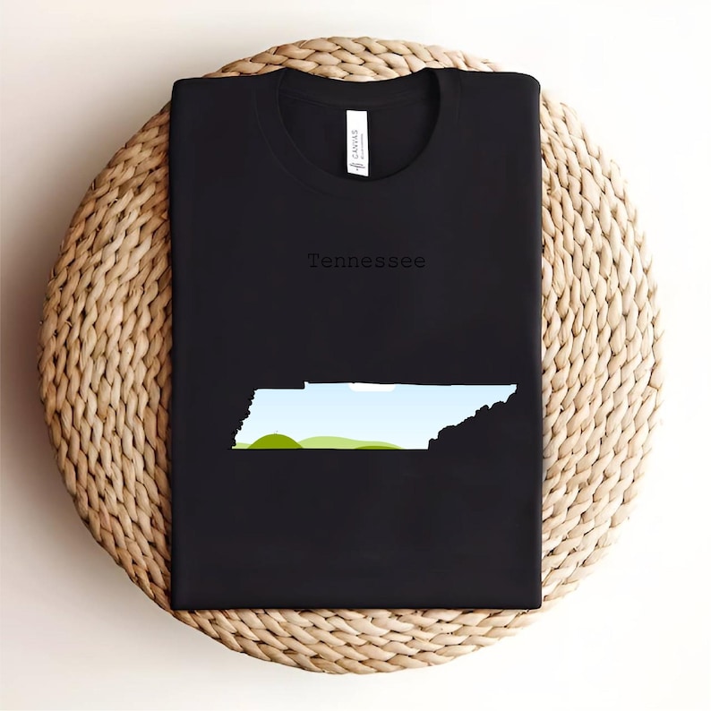May include: Black t-shirt featuring the state of Tennessee in a minimalist design. The state outline is filled with a landscape of green hills and blue sky. The word "Tennessee" is printed above the state outline.